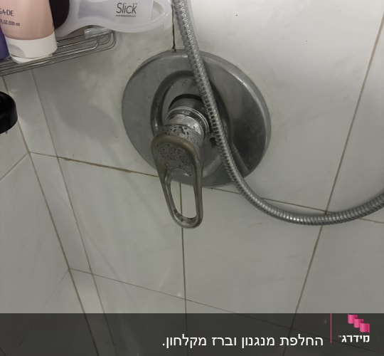 ברז מקלחת עם צינור מתכת על קיר אריחים לבנים